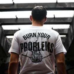 Man standing indoors, wearing a t-shirt with 'Burn Your Problems' text, viewed from behind.